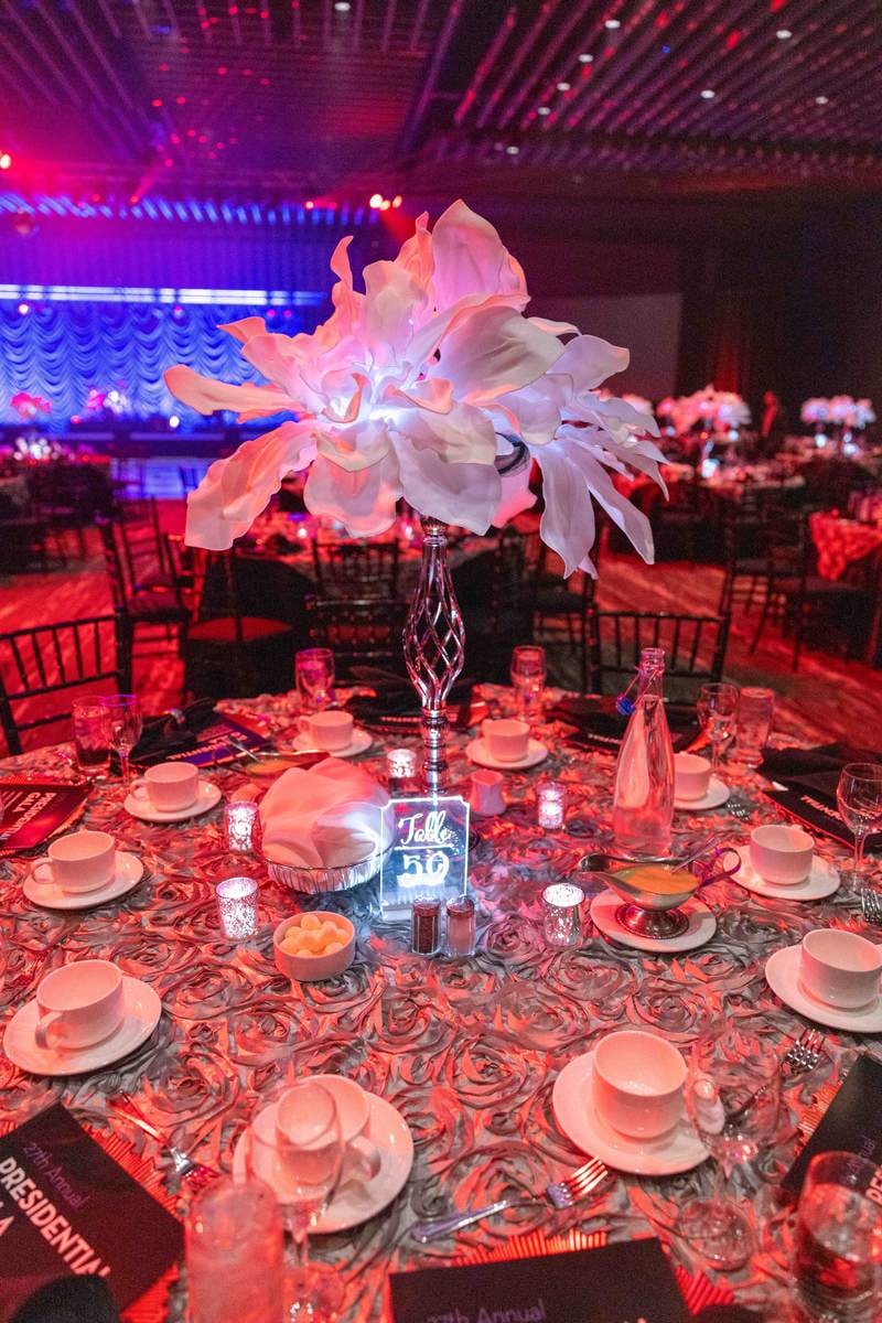 Feathered white centerpiece over a dinner table in red and purple ballroom light