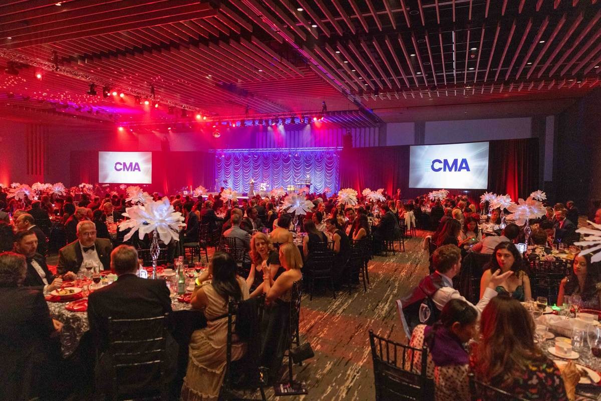 Wide view of the ballroom with guests seated at round tables under CMA screens