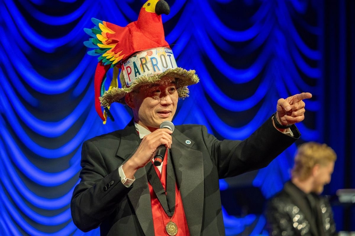 Sing-along leader in a colorful parrot hat performing on stage under blue lights