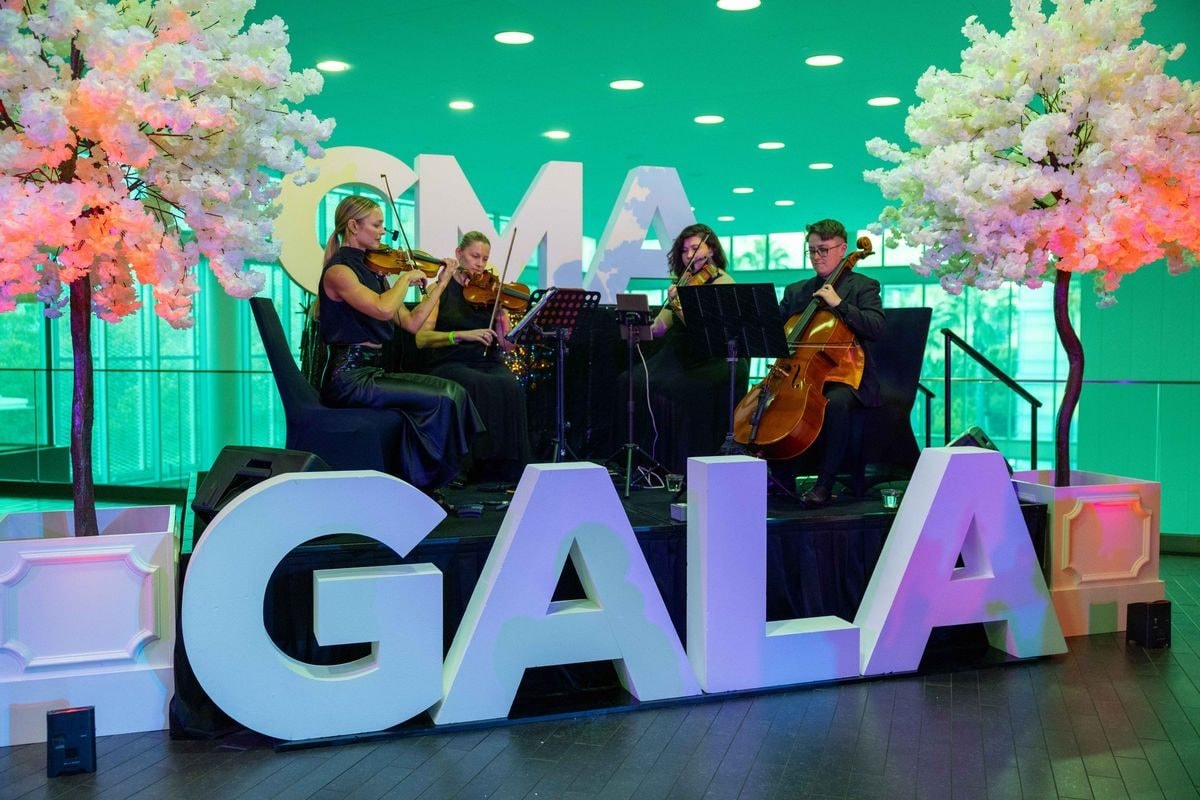 String quartet playing beside giant CMA GALA letters and blossom trees at the reception