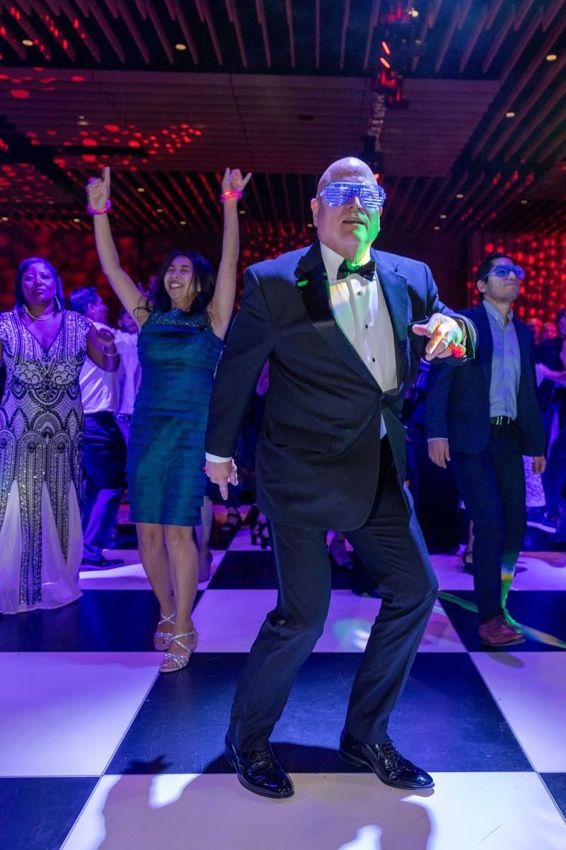 Guest in a tuxedo dancing on the checkerboard floor as others cheer behind him