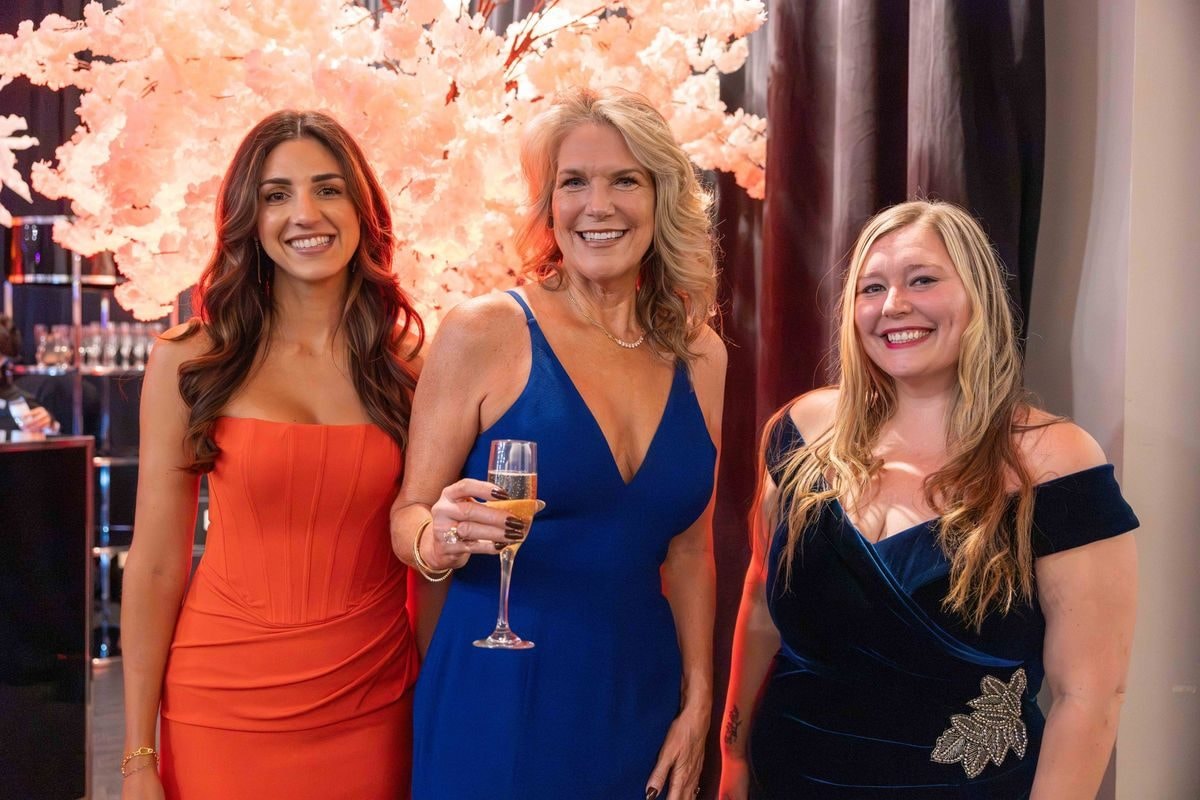Three guests in evening gowns posing under blossom trees at the reception