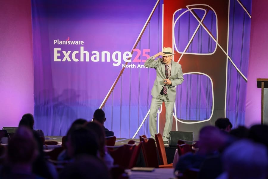 Speaker on the Planisware Exchange 25 stage addressing a packed ballroom in San Francisco — corporate event photography by Michael Pegram