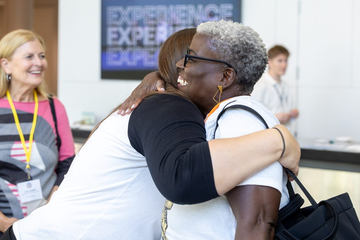 Two attendees hugging hello at registration at the CA RISE conference in San Francisco — corporate event photography by Michael Pegram