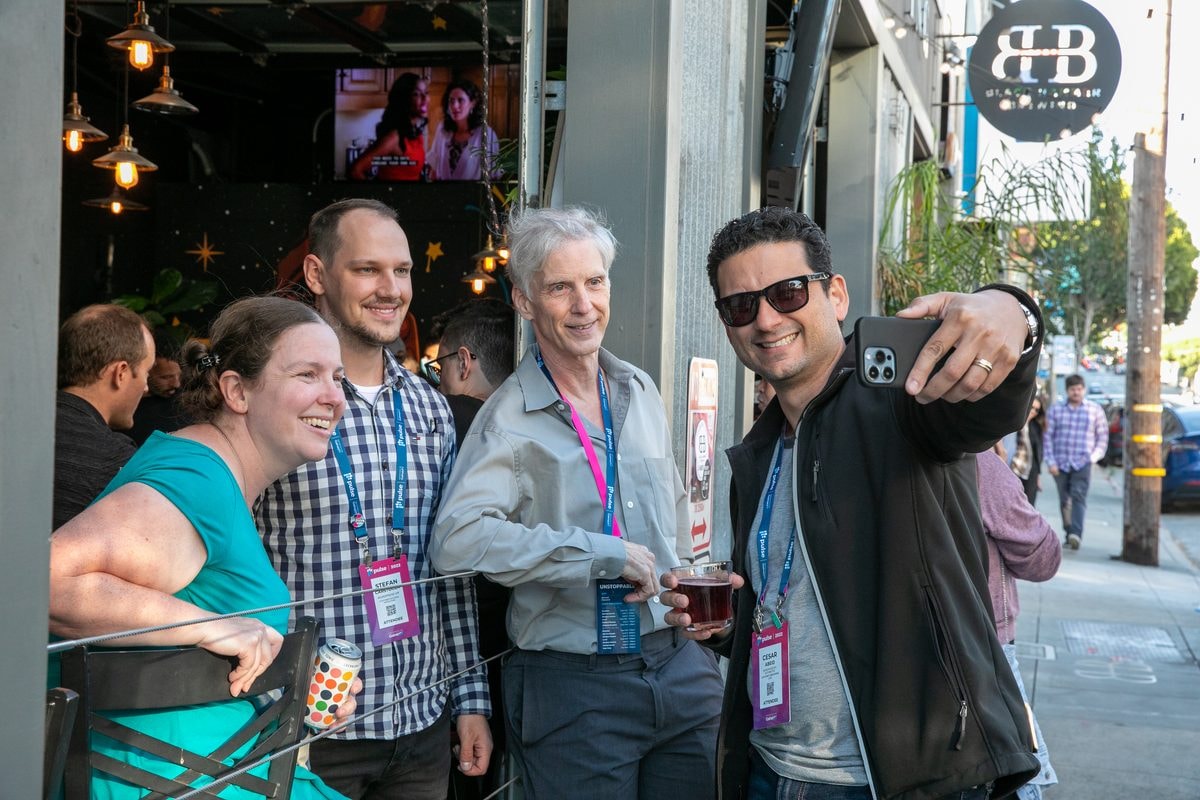 Conference attendees taking a group selfie at an outdoor networking happy hour in San Francisco — corporate event photography by Michael Pegram