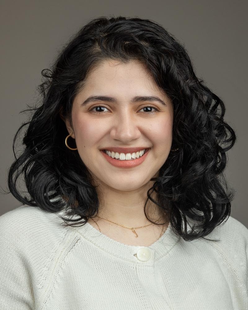 Corporate headshot of a smiling young professional woman with curly dark hair on a grey backdrop — San Francisco headshot by Michael Pegram