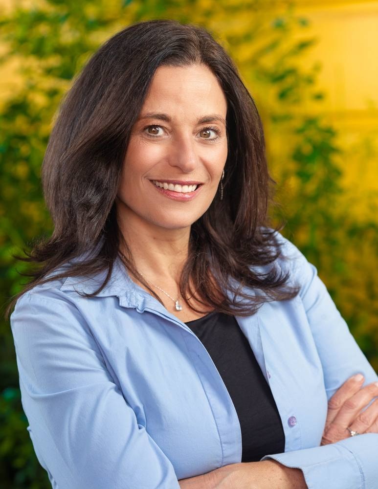 Outdoor portrait of a smiling businesswoman in a light blue blouse with arms crossed — headshot by Michael Pegram